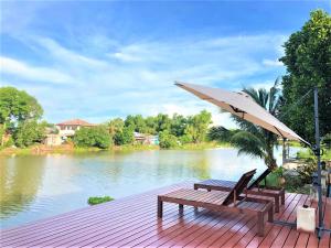 a wooden deck with two benches and an umbrella at Thararin Villa in Ban Doem Bang