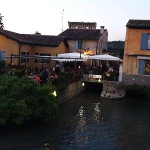 ein Restaurant neben einem Fluss mit Menschen, die auf einer Brücke sitzen in der Unterkunft Corte La Guarnigione in Valeggio sul Mincio
