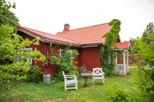 uma casa vermelha com duas cadeiras brancas em frente em Westergårds em Föglö