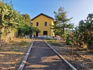 a road leading to a yellow house with trees at Le Case del Parco in Peschici +8 photos