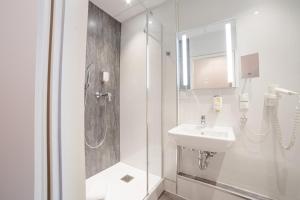 a white bathroom with a sink and a shower at City Hotel Hannover in Hannover