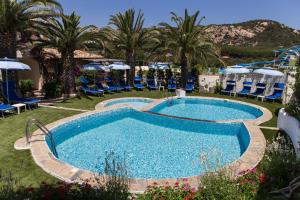 uma piscina num resort com palmeiras e cadeiras em La Jacia Hotel & Resort em Baja Sardinia