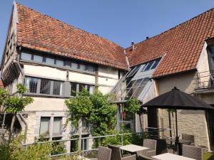 un patio con mesas y una sombrilla frente a un edificio en Aparthotel De Beek Anno 1410, en Sint-Truiden