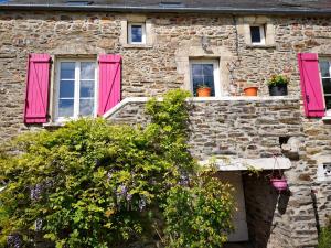 Crasville的住宿－Au Domaine de Sophie piscine chauffée couverte et jacuzzi couvert，一座石头建筑,设有粉红色百叶窗和鲜花