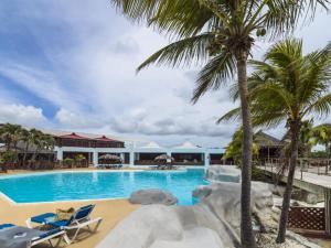 a resort swimming pool with palm trees and chairs at STUDIO DJANGO in Saint-François