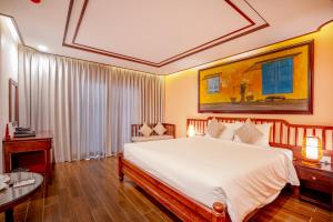 a bedroom with a large white bed and a table at Fivitel Hoi An Hotel in Hoi An