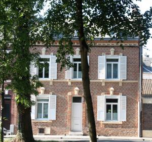 アミアンにあるLe Kiosque Amiens chambres d'hôtesの白い窓と木々が並ぶ古いレンガ造りの建物