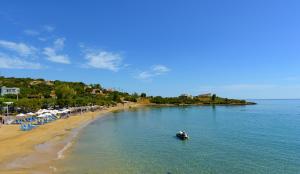 un barco en el agua en una playa con sombrillas en Ammoudara Beach Hotel Apartments, en Agios Nikolaos