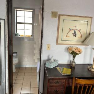 a bathroom with a toilet and a table with a vase of flowers at Cottonwood Court Motel in Santa Fe