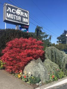 una señal para una posada con flores rojas y una roca en Acorn Motor Inn, en Oak Harbor