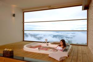 Amber Dale Luxury Hotel & Spa, Munnar في مونار: امرأة جالسة في حوض الاستحمام في غرفة مع نافذة كبيرة