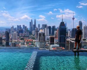 Ein Mann steht am Rande eines Gebäudes mit Blick auf eine Stadt. in der Unterkunft Regalia Residence The Sky Pool Suite in Kuala Lumpur