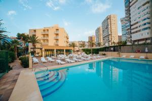 a swimming pool with white lounge chairs and buildings at Apartamentos Palm Court in Benidorm