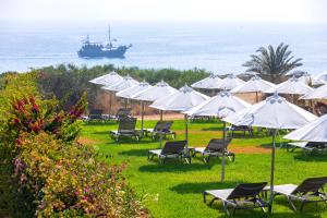 a group of chairs and umbrellas with a ship in the ocean at Leonardo Crystal Cove Hotel & Spa – Adults only in Protaras