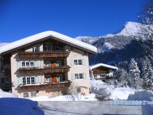 a building in the snow with mountains in the background at Hotel Garni Ingeborg in Mittelberg