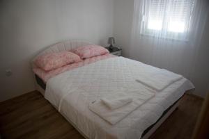 a bed with white sheets and pink pillows and a window at Apartman Miloš in Trebinje