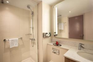 uma casa de banho com um chuveiro, um lavatório e um espelho. em Leonardo London Heathrow Airport em Hillingdon