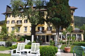 a yellow building with two white chairs and trees at Strandhotel Prinz in Ossiach