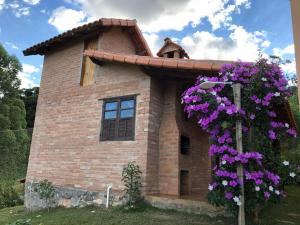 a small brick house with purple flowers in front of it at Chalé Ibiti in Conceição da Ibitipoca