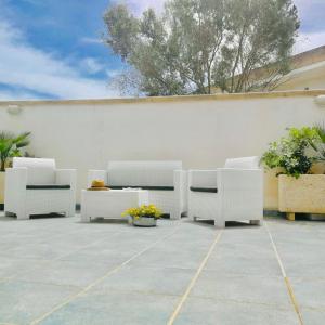 a patio with white chairs and plants and a white wall at Residence Le Palme in Marina di Mancaversa