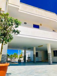 un gran edificio blanco con árboles delante de él en Residence Le Palme, en Marina di Mancaversa