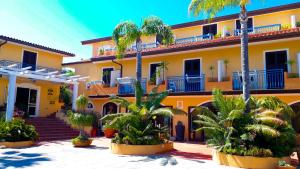 a yellow building with palm trees in front of it at Hotel Grotticelle in Capo Vaticano