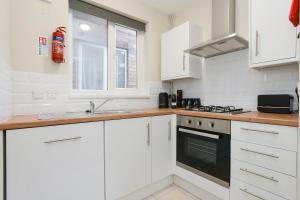 een keuken met witte kasten, een wastafel en een fornuis bij Cosy House in the heart of Beeston with FREE Parking and WiFi in Nottingham