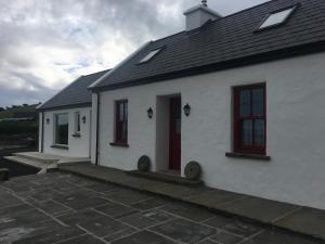 a white house with red windows and a patio at Conway's Cottage with Sea View Nestling by Cliffs-of-Moher in Liscannor