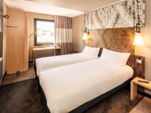 a hotel room with a large white bed and a window at ibis Pontorson Baie Du Mont Saint Michel in Saint-Georges-de-Gréhaigne