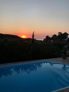 a sunset over a swimming pool with the sun setting at Villa Helios in Pefkochori