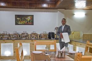 Un uomo in piedi in un ristorante con un giornale in mano di Hotel Hayer Regency a Manāli