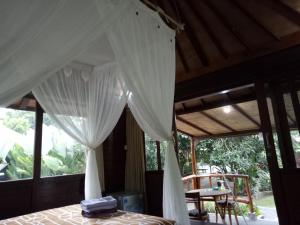 a bedroom with a bed with curtains and a table at Mulia Home Stay in Nusa Dua
