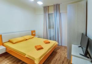 a bedroom with a bed with yellow sheets and a television at Apartments Harmonia Colours in Budva