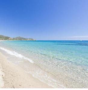 a beach with blue water and trees in the background at Splendida villetta Kal'e Moru in Marongiu