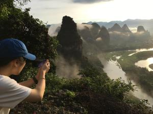 a person taking a picture of a river and mountains at Yangshuo Yunshe Mountain Guesthouse in Yangshuo
