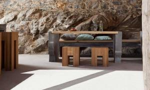 a wooden table with benches and a rock wall at Coco-Mat Eco Residences Serifos in Vayiá