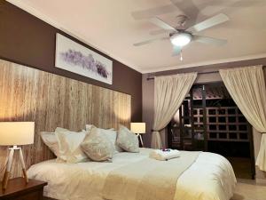 a bedroom with a white bed with a ceiling fan at The Wilds Guest House in Hluhluwe