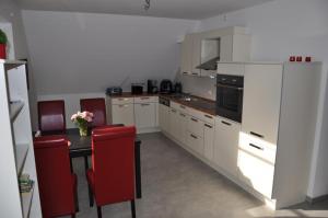 a kitchen with white cabinets and a table with red chairs at Ferienwohnung Kaplan in Bad Zwischenahn