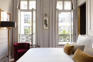 a bedroom with a white bed and a chair and windows at Les Jardins du Faubourg Hotel & Spa by Shiseido in Paris
