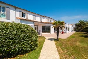 a building with a palm tree next to a sidewalk at Thalacap Île de Ré - Thalasso & Spa in Ars-en-Ré