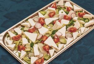 a tray filled with a salad with cheese and tomatoes at Lavender Villa in Mamaia Sat/Năvodari