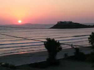 a sunset on the beach with a house on an island at Infinity Apartments in Naxos Chora