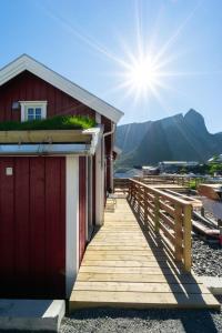 a wooden boardwalk leading to a building with the sun in the background at Madelhea Cabin- Seaview Lodge in Reine