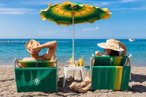 two people sitting on the beach under an umbrella at Hotel Savojo in Petrovac na Moru
