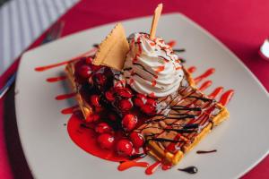 a waffle with whipped cream and berries on a plate at Hotel Savojo in Petrovac na Moru
