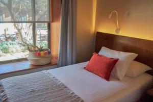 a bed with a red pillow next to a window at Hotel La Casa de Don Tomás in San Pedro de Atacama