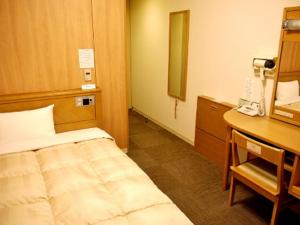 a room with a bed and a desk with a phone at Hotel Route-Inn Tomakomai Ekimae in Tomakomai
