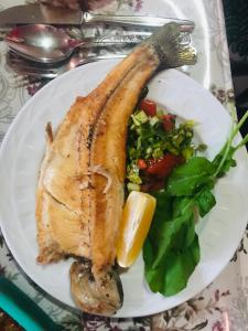 un plato de comida con un trozo de pescado y verduras en ZÜMRÜT PANSİYON Side en Side