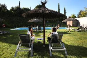 dos mujeres sentadas en sillas de césped bajo una sombrilla en Hotel Món Sant Benet, en Sant Fruitós de Bages