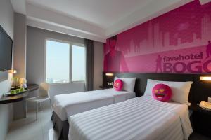 two beds in a hotel room with a pink wall at favehotel Padjajaran Bogor in Bogor